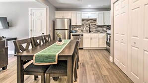 A modern kitchen with white cabinets, a stainless steel refrigerator, and a wooden dining table with chairs. - Airy Townhome: Close to Kayaking & Boating! (Kimberling City)