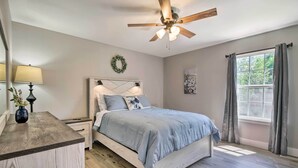 A bedroom with a bed, a nightstand, a lamp, a ceiling fan, a window with curtains, and a wall-mounted artwork. - Airy Townhome: Close to Kayaking & Boating! (Kimberling City)
