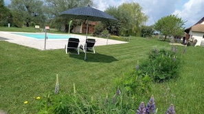 Ein Garten mit Swimmingpool, zwei Liegestühlen und Sonnenschirm.