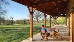 Een overdekt terras met houten meubels en uitzicht op een grasveld.