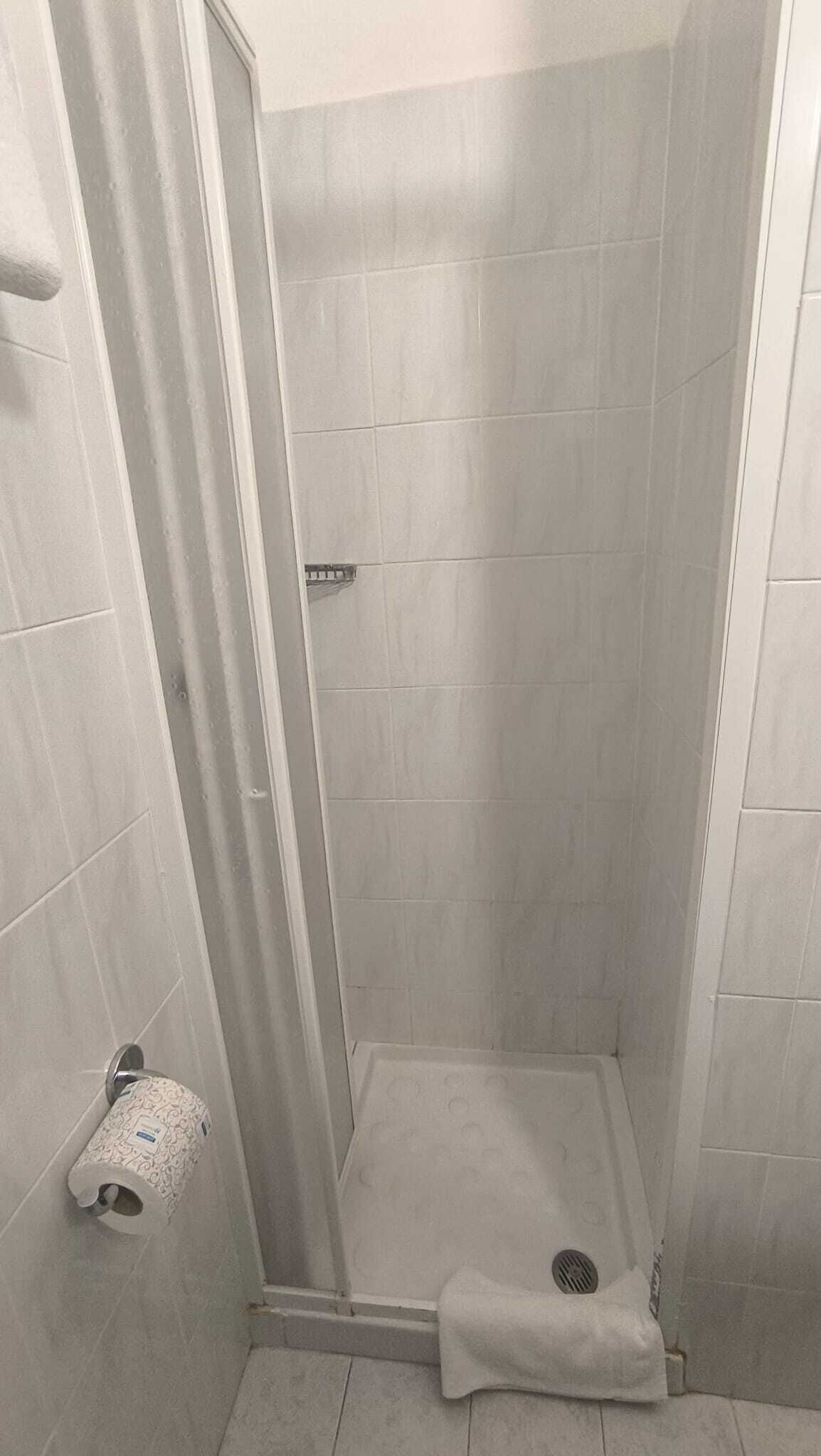 A small, enclosed shower area with tiled walls and floor, a shower curtain, and a towel on the floor.