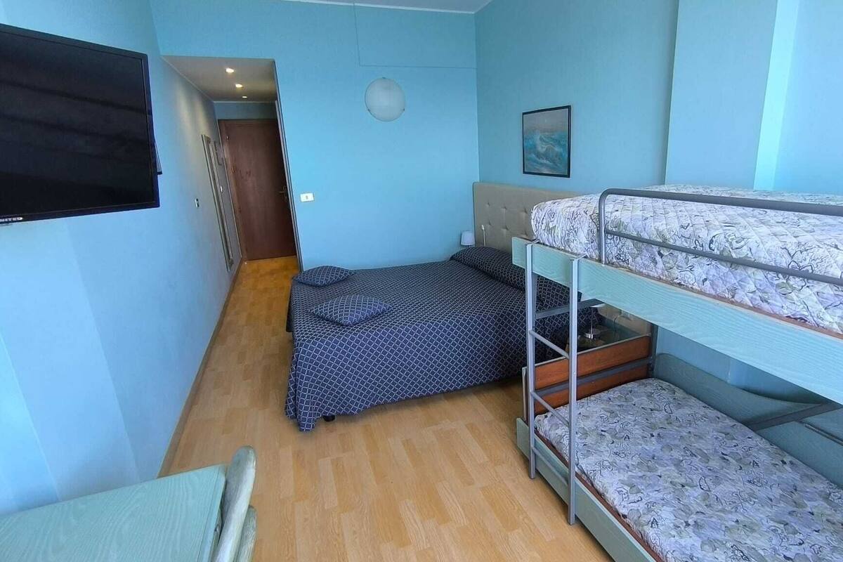 A compact room with a bunk bed, a single bed, a desk, and a television.