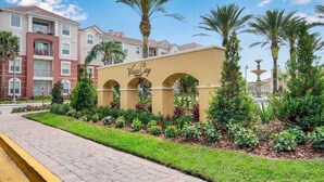 A resort named Vista Cay with a central archway, surrounded by well-maintained gardens and palm trees. - Cozy 3BR Apartment - Vista Cay Resort near Disney! (Orlando)