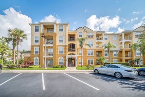 A multi-story residential building with balconies, a central entrance, and a parking lot.