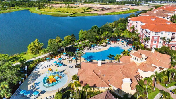A resort with a central pool, a water park, and a view of a lake and city skyline. - Cozy 3BR Apartment - Vista Cay Resort near Disney! (Orlando)