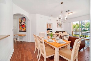 A dining area with a wooden table set for four, surrounded by white chairs.