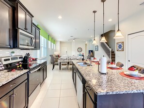 A modern kitchen with dark cabinetry, a large island with a sink, and a dining area with a white table and chairs. - Cozy 5-Bedroom Home with Private Pool (Four Corners)