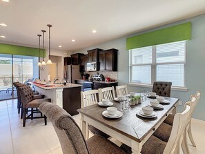 A modern kitchen with dark cabinets, a central island, and a dining area with a wooden table set for four. - Cozy 5-Bedroom Home with Private Pool (Four Corners)
