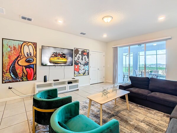 A living room with a flat-screen TV, two green armchairs, a coffee table, and a dark sofa.