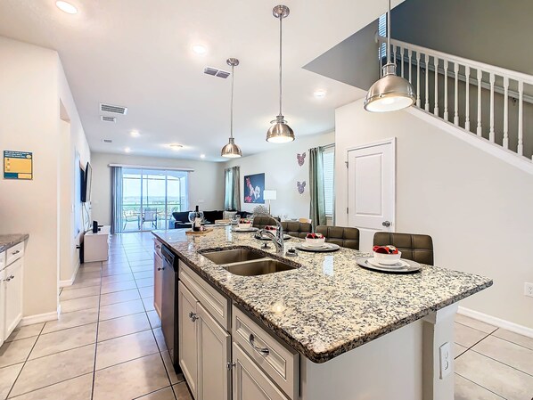 A spacious kitchen with a large island, modern pendant lights, and a view to the outside.