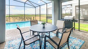 Un patio con piscina, una parrilla y una mesa con sillas.