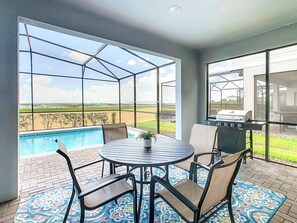 A patio with a pool, a grill, and a table with chairs.