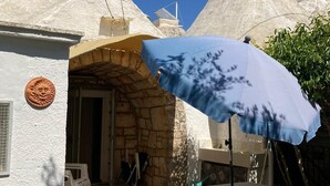 Een stenen gebouw met een witte gevel, een blauwe parasol en een kleine tafel.