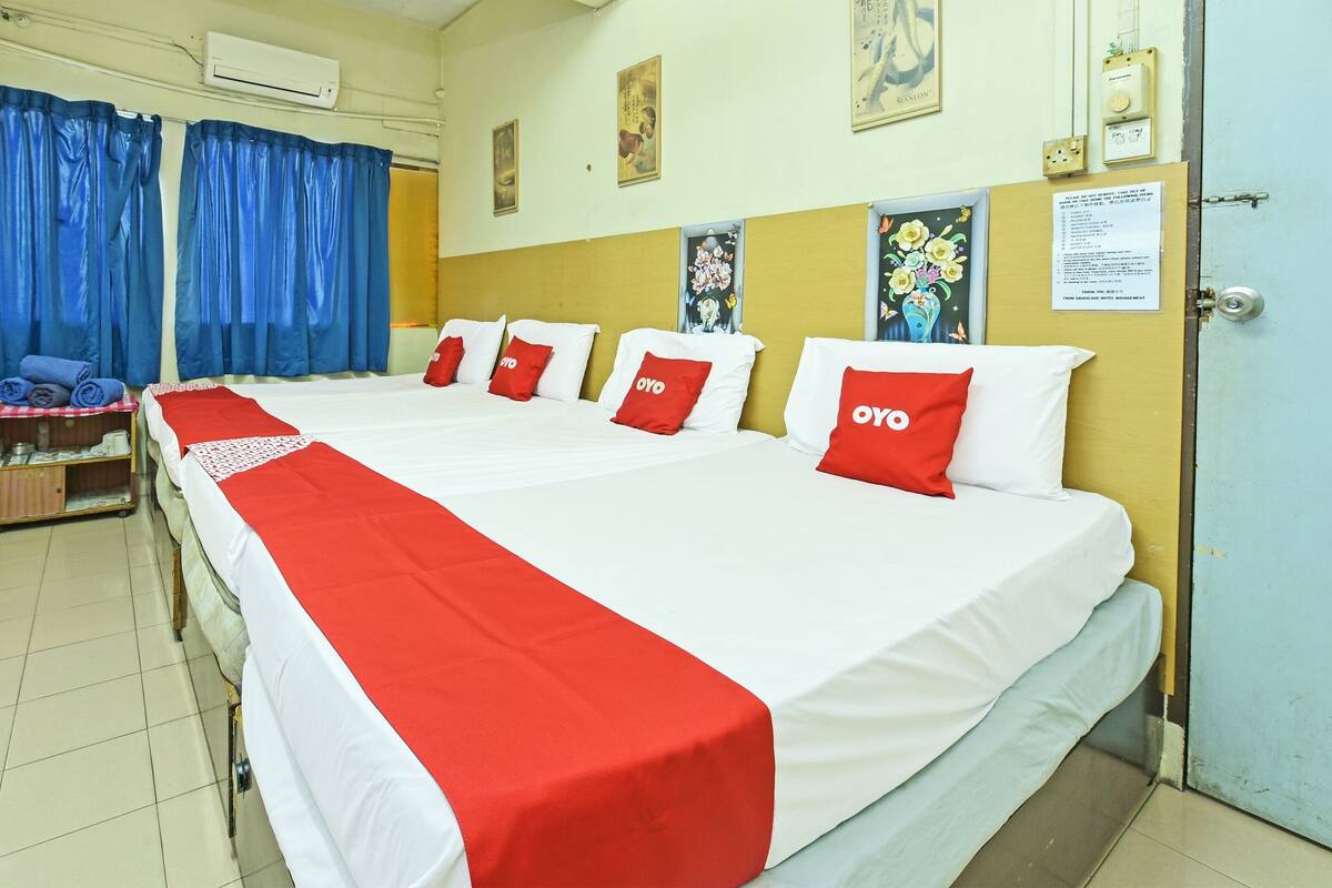 Quarto de hotel com uma cama grande, roupa de cama vermelha e branca, e cabeceira de madeira.