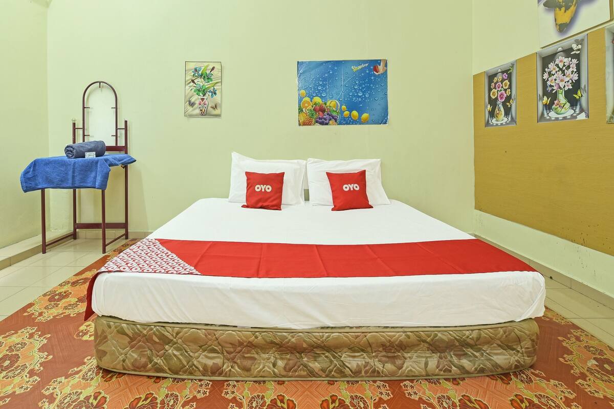 Uma cama bem arrumada com roupa de cama vermelha e branca, uma toalha azul em um suporte e um espelho na parede.