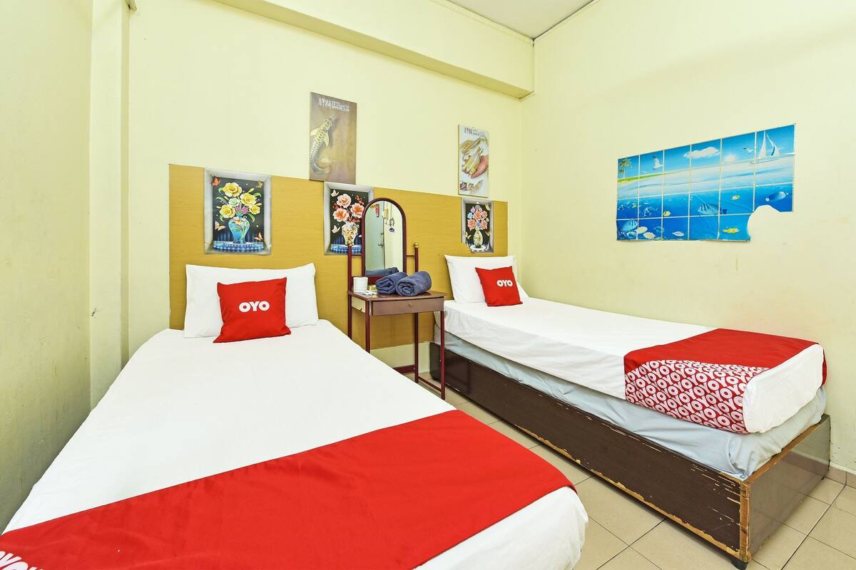 Quarto de hotel com duas camas, cada uma com colcha vermelha e branca, uma mesinha com espelho e decorações nas paredes, incluindo um mapa e arte floral.