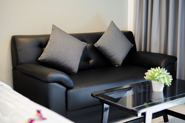 A black leather sofa with two grey cushions, a glass coffee table, and a white vase with flowers. - DEL MAX resort Pattaya (Pattaya)