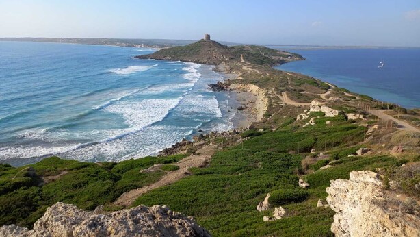 Un paysage côtier caractérisé par une colline imposante surmontée d’une construction, un littoral accidenté et une vue dégagée sur la mer.