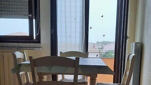 Un espace repas comprenant une table et des chaises, une fenêtre avec des stores et une vue sur l’extérieur.