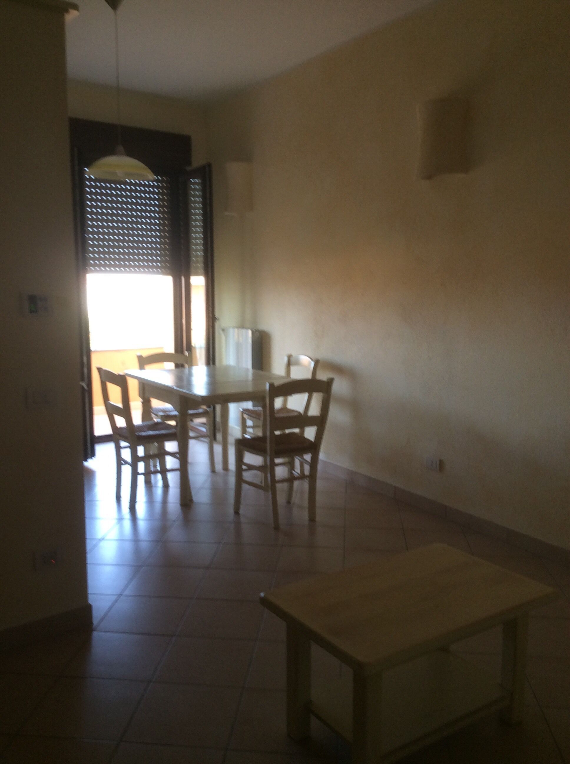 A dining area with a round table and four chairs, a small rectangular table, and a window with blinds.