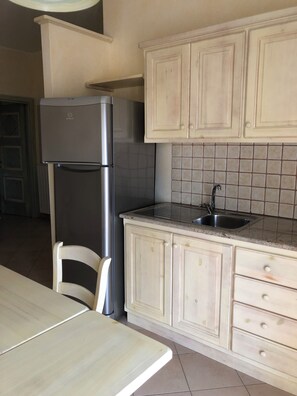 A kitchen with a refrigerator, sink, and cabinets. - Spacious two-room apartment located on the first floor, with a balcony and a bathroom. (Cabras)