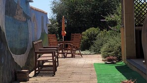 Une terrasse extérieure agrémentée d’une fresque murale, de meubles en bois et de plantes en pot.