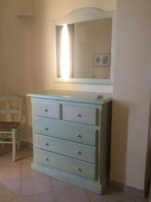 A white dresser with a mirror above it, a chair to the left, and a framed picture on the wall. - Large two-room apartment on the first floor, with balcony and bathroom.  (Cabras)