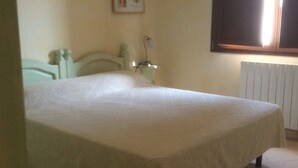 Une chambre à coucher avec un lit, une table de chevet, une lampe, un radiateur et une fenêtre.