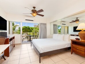 A hotel room with a bed, a desk, a chair, a television, a ceiling fan, and a balcony with a view of greenery. - Park Views w/Kitchenette, Lanai - Waikīkī Shore #415 (Honolulu)