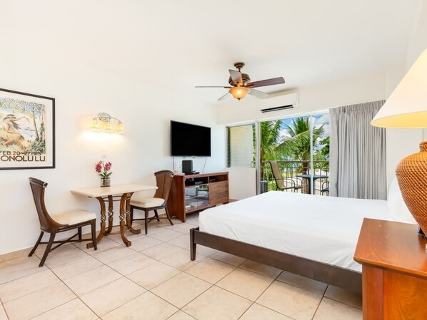 A hotel room with a bed, desk, chair, TV, and a balcony with a view of palm trees. - Park Views w/Kitchenette, Lanai - Waikīkī Shore #415 (Honolulu)