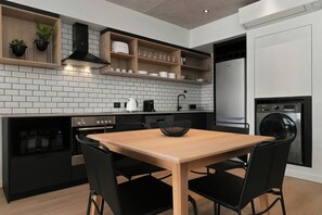 A modern kitchen with a wooden table, black chairs, a built-in oven, and a washing machine.