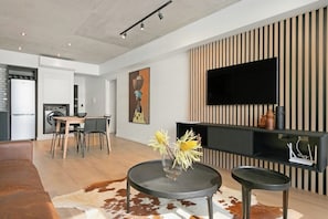 A modern living room with a flat-screen TV, a dining area, and a sofa.