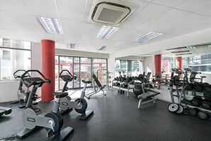 Ein Fitnessraum mit Trainingsgeräten, großen Fenstern und einer roten Säule.
