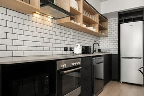 A modern kitchen with white tiled backsplash, stainless steel appliances, wooden shelves, and a built-in oven.