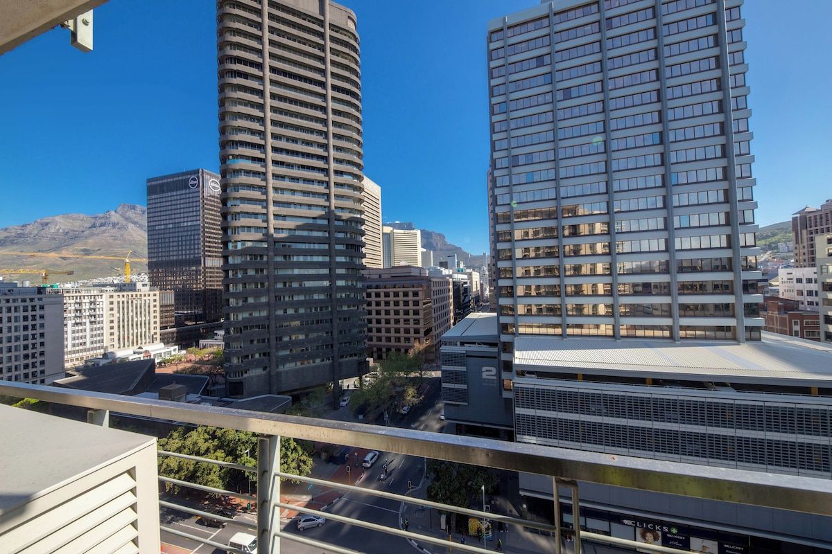 Un edificio alto con fachada curva, una estructura de techo plano con una cuadrícula de ventanas y una vista despejada del paisaje urbano circundante.