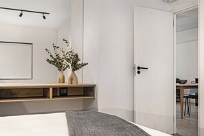 A modern bedroom with a bed, bedside tables, a nightstand, a mirror, and a door leading to another room.