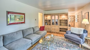 Ein Wohnzimmer mit grauem Sofa, einem Glastisch, einem gemusterten Teppich und einer Vitrine mit Glastüren.