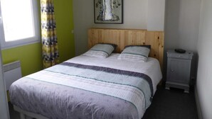 Un dormitorio con cama, mesita de noche, ventana con cortinas y una obra de arte colgada en la pared.