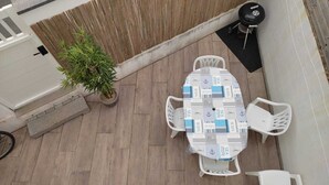 Un patio con una mesa, sillas, una planta en maceta y una parrilla.