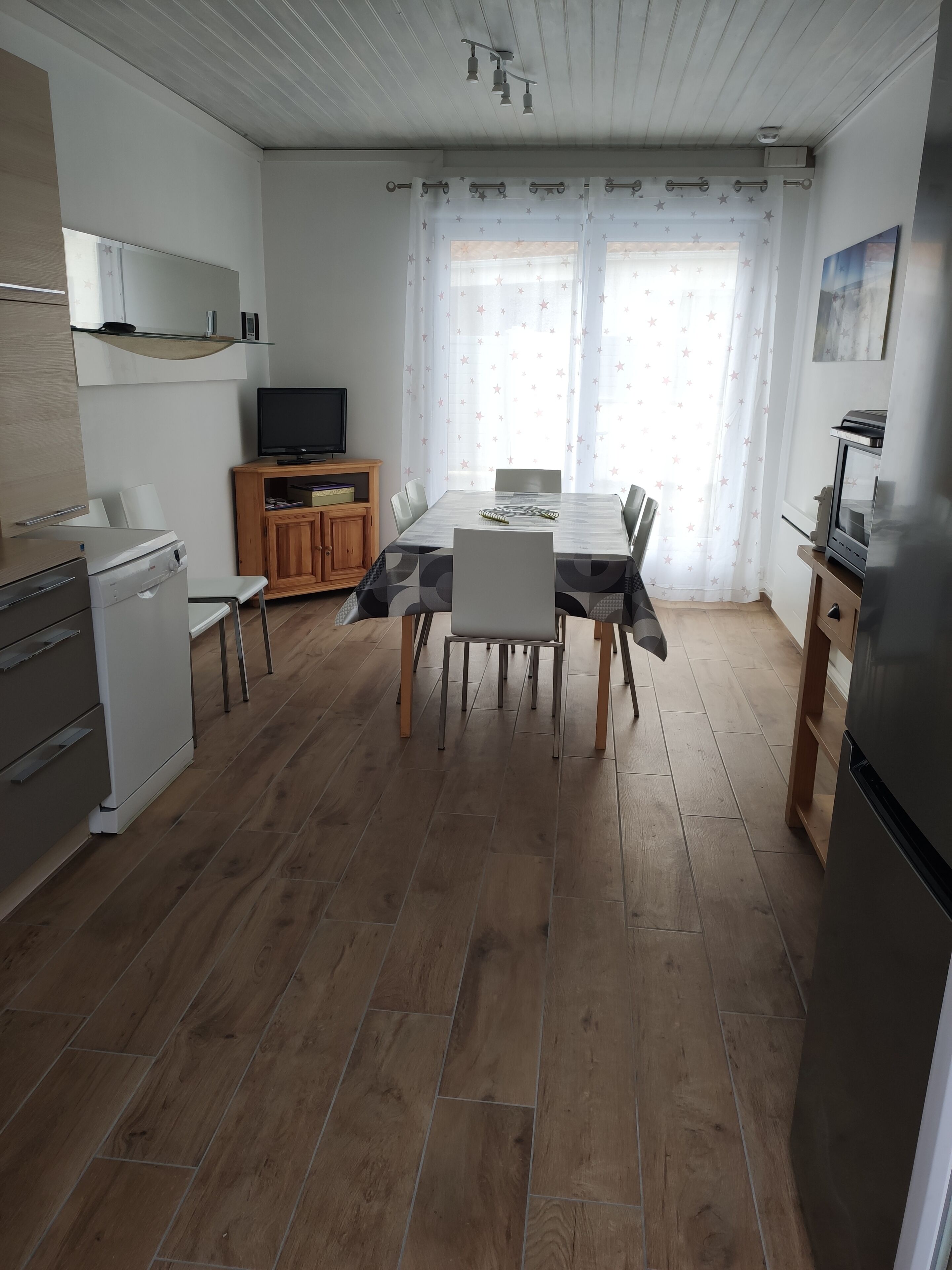 Una cuina moderna amb zona de menjador, terres de fusta i un televisor.