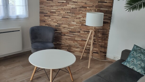 Una sala de estar moderna con una pared de madera, un sofá gris, una mesa redonda blanca y una lámpara de pie.