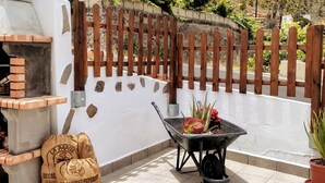 Ein Terrassenbereich im Freien mit einem Backofen aus Ziegeln, einem Schubkarren mit Gartenwerkzeugen und Säcken voller Erde.