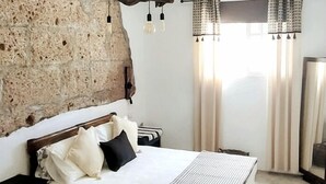 Ein Schlafzimmer mit einer Steinsäule, einem Bett mit weißer Bettwäsche und schwarzen Kissen, einem Nachttisch und einer Hängeleuchte.