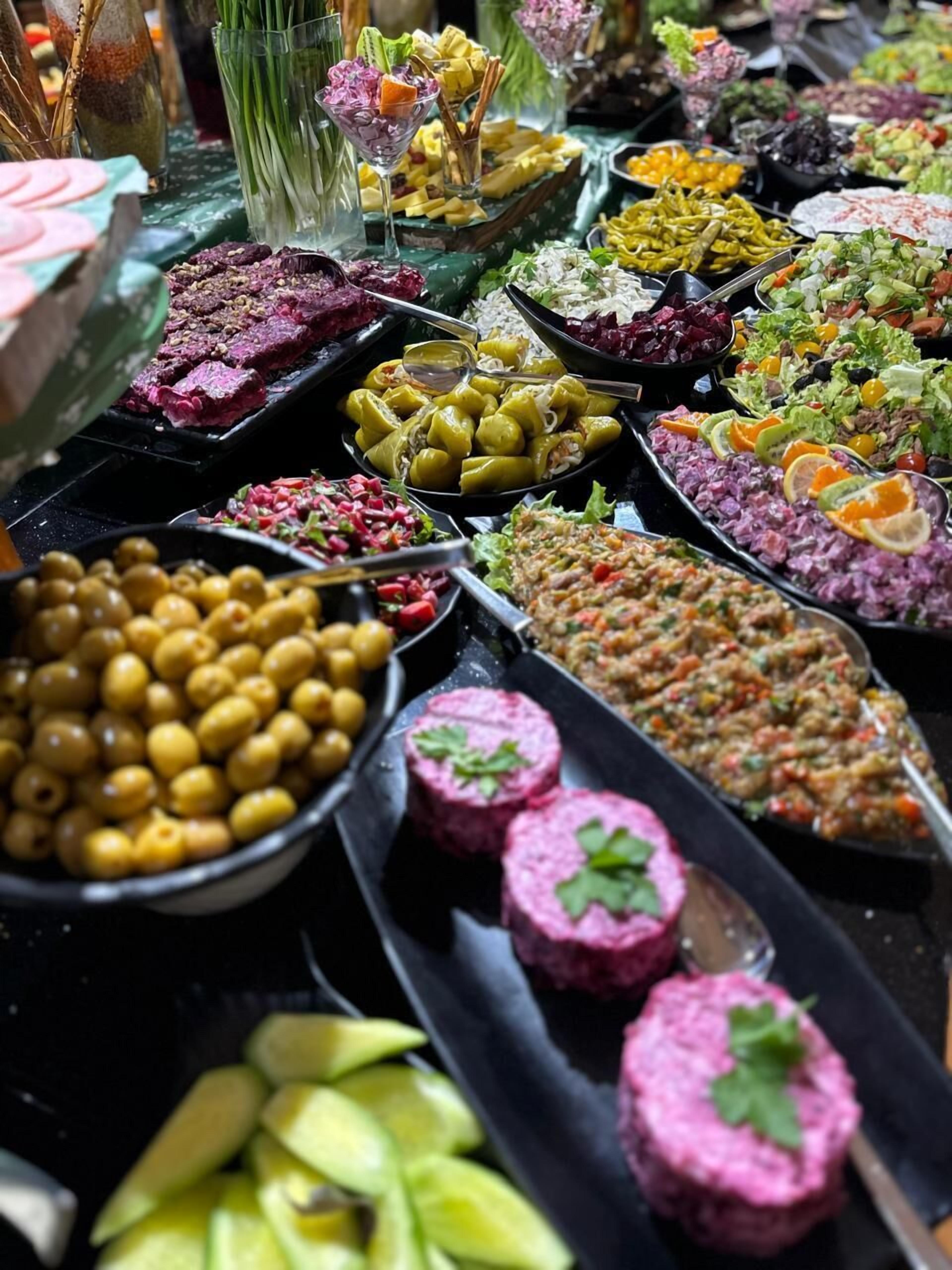 Un bufé con diversos platos, entre ellos aceitunas, verduras encurtidas y carne.
