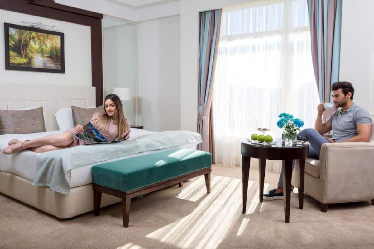 A hotel room with a bed, a sofa, a small table with a vase and apples, and a window with curtains.