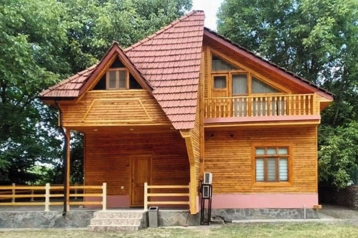 A wooden cabin with a red roof, a balcony, and a stone foundation.