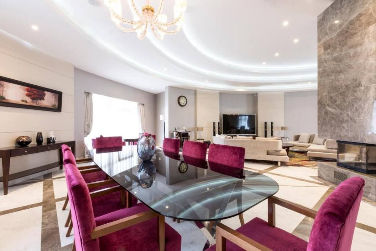 A modern living room with a glass-top dining table, red upholstered chairs, a large flat-screen TV, and a stone accent wall.
