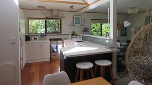 A modern kitchen with a central island, wooden flooring, and a hanging light fixture.