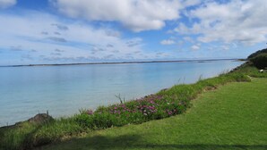 A coastal landscape with a grassy area, a body of water, and a distant shoreline.