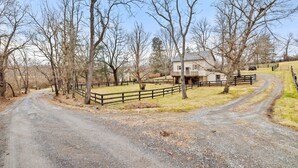 A rural property with a dirt road, wooden fences, and leafless trees.